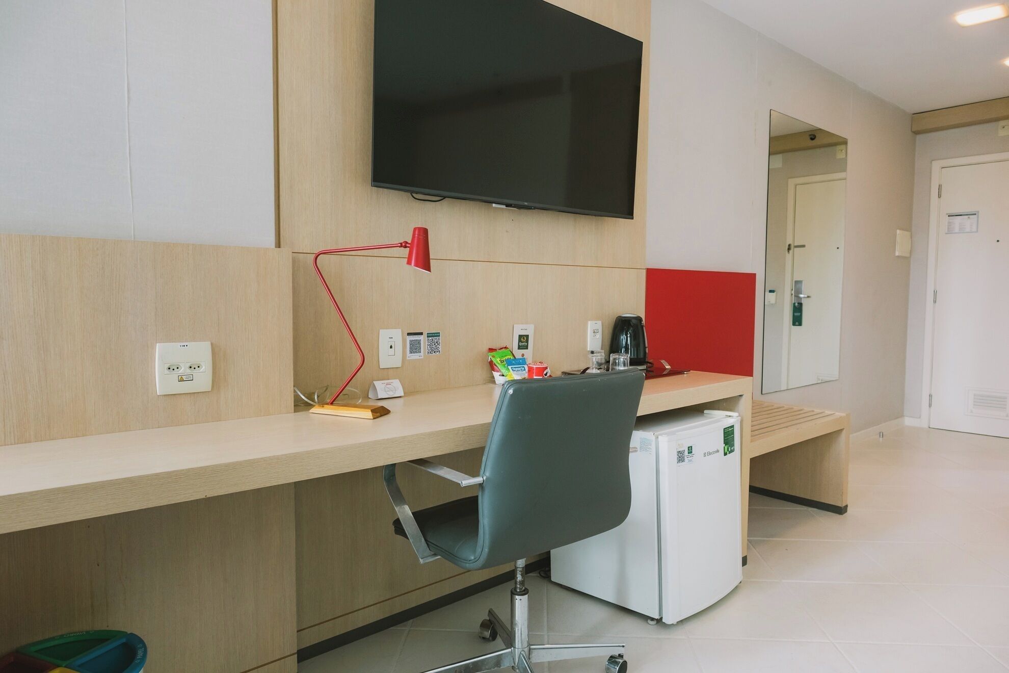 A modern office space with a desk, chair, and a flat-screen TV mounted on the wall.