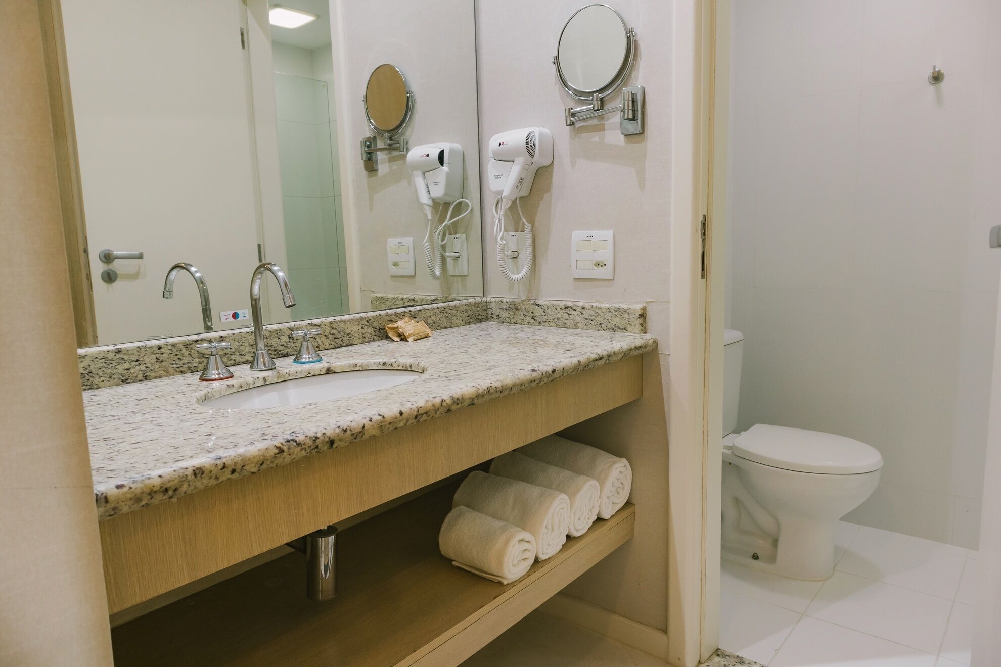 Un baño con lavamanos de granito, un espejo, un secador de pelo y un inodoro.