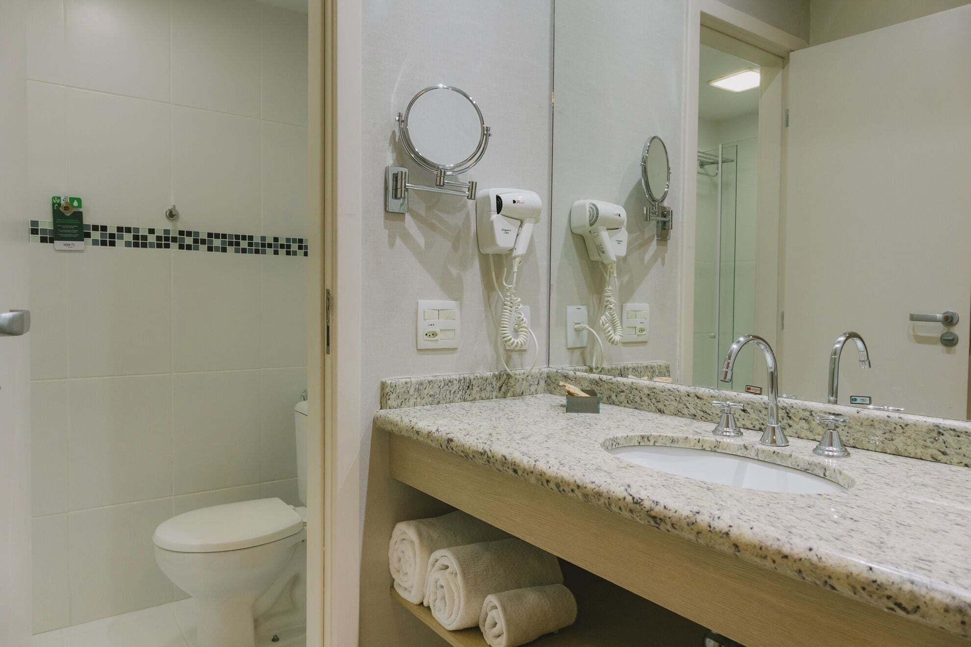 Un baño con inodoro, dos secadores de pelo, un lavabo con encimera de mármol y un espejo.