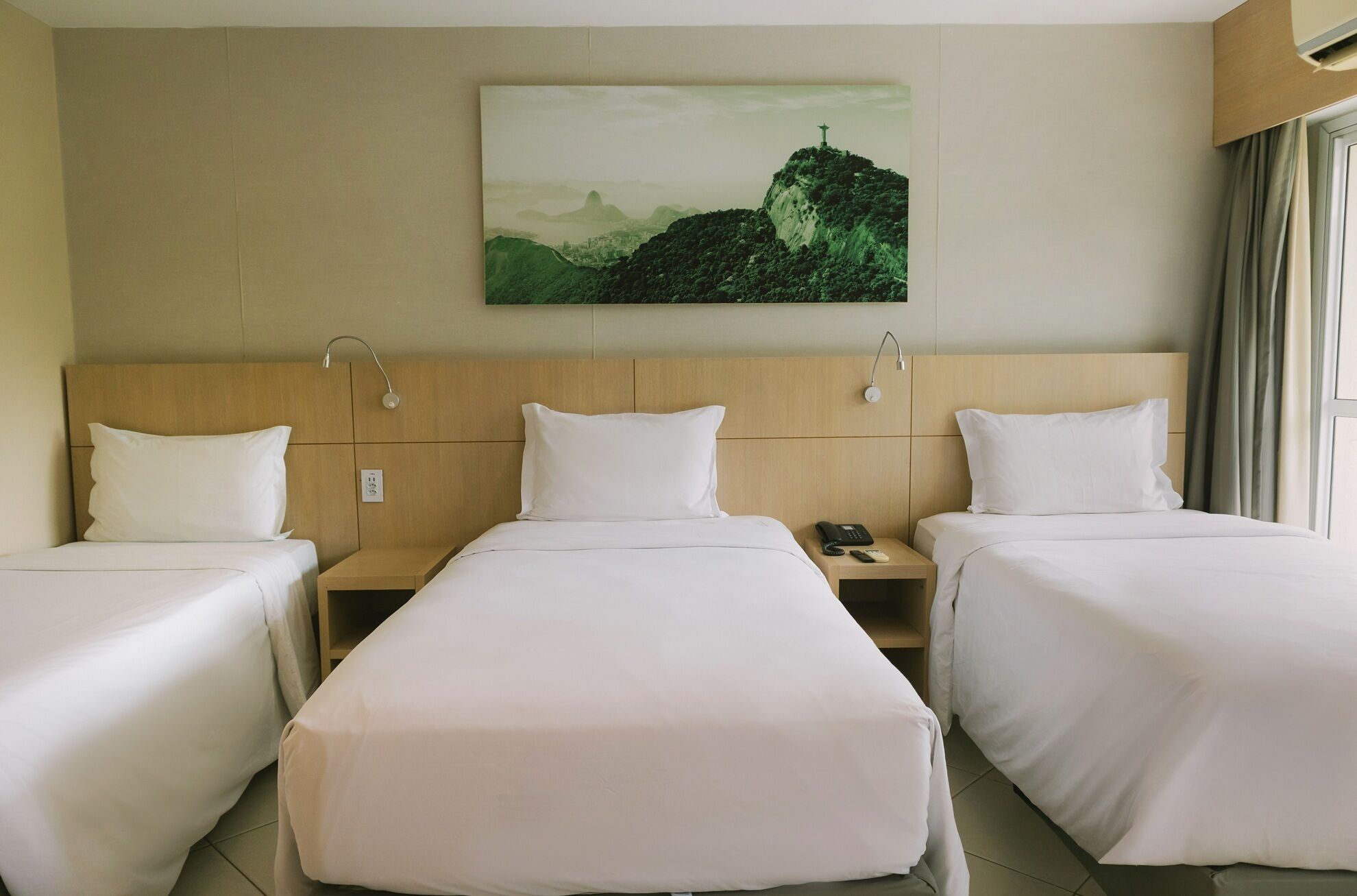 A hotel room with two beds, a headboard, bedside tables, a phone, and a painting of a landscape.