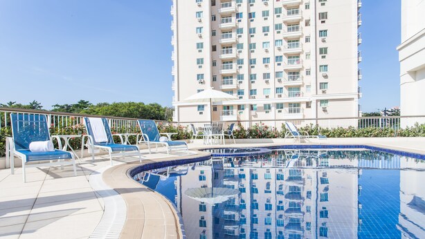 Una piscina con sillas de descanso y un rascacielos al fondo.