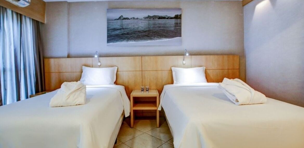 Habitación de hotel con dos camas, una mesita de noche y un cuadro de una escena costera.