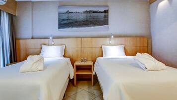 Habitación de hotel con dos camas, una mesita de noche y un cuadro de una escena costera.