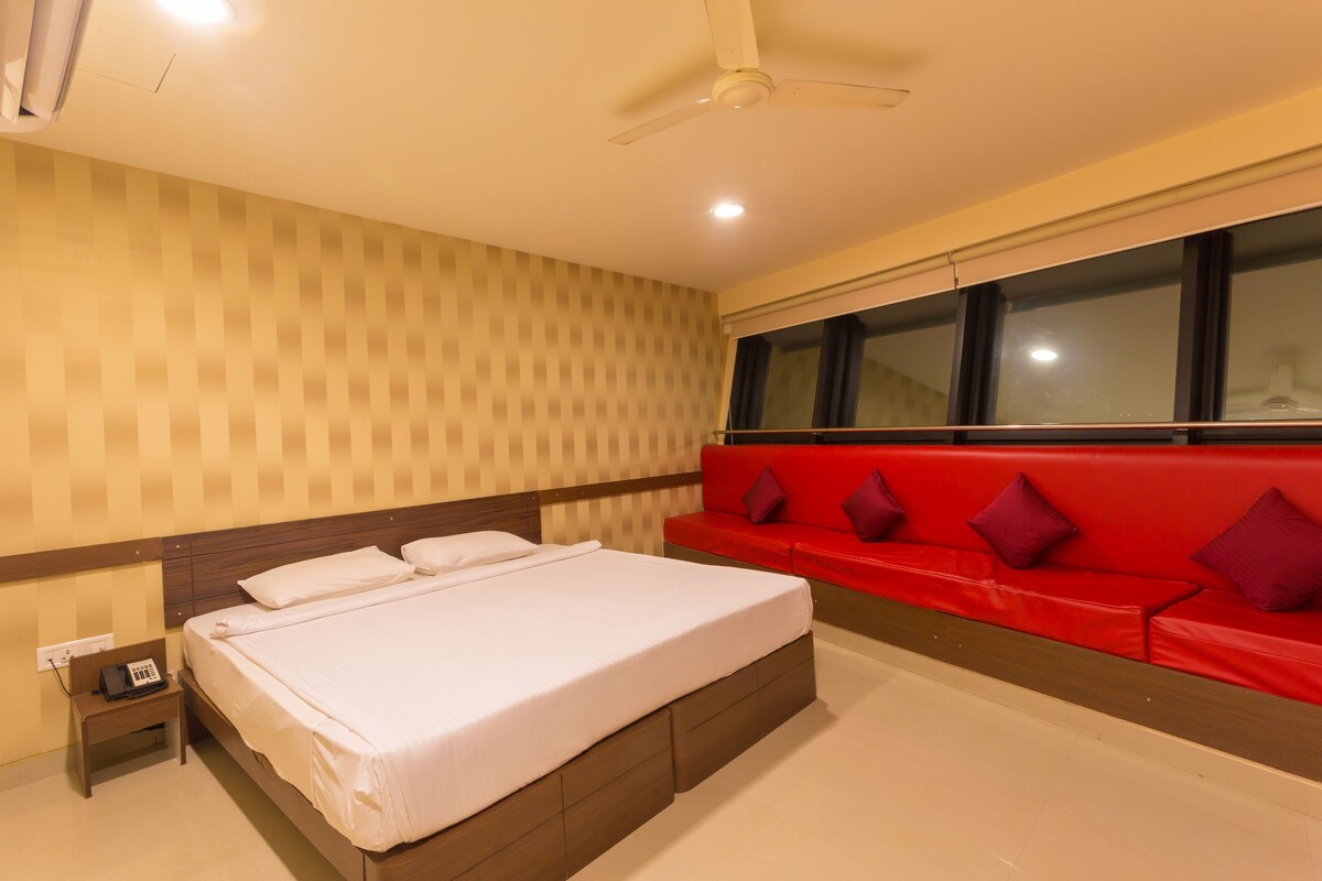 Habitación de hotel con una cama, un sofá rojo, una ventana y un ventilador de techo.