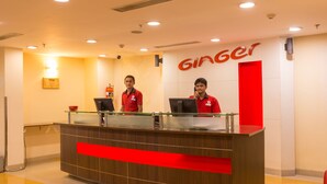 A reception desk with two staff members in red uniforms, a glass partition, and a 'Ginger' sign on the wall. - Ginger Chennai Vadapalani (Chennai)