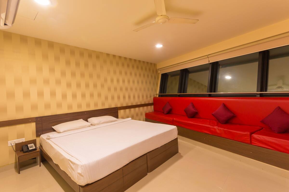 A hotel room with a bed, a red sofa, a window, and a ceiling fan.