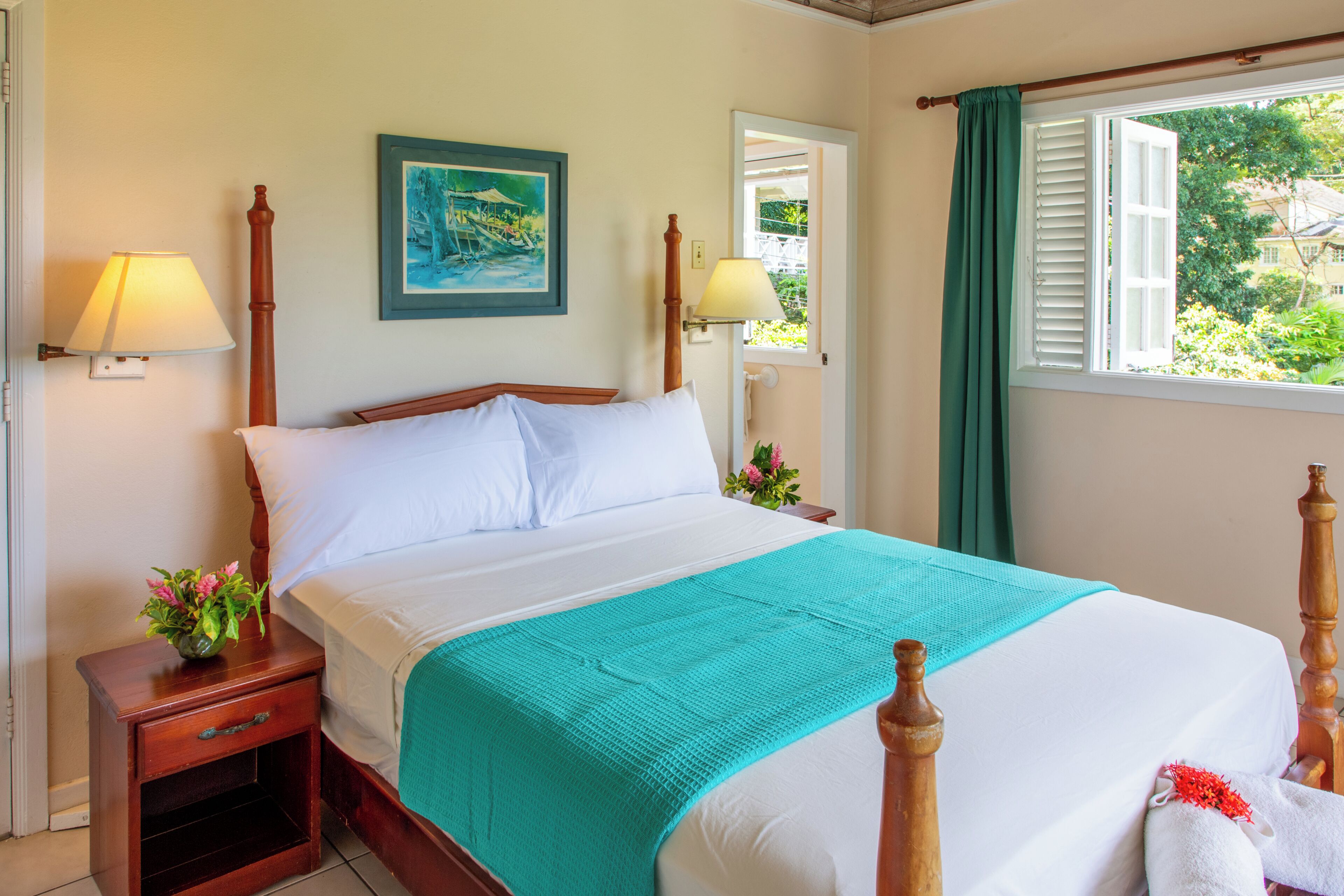 Un lit bien fait, recouvert d’une couvre-lit turquoise, avec deux lampes de chevet, un tableau encadré au mur et une fenêtre avec des rideaux.