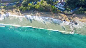 Eine Luftaufnahme eines Strandes mit klarem türkisblauem Wasser, einem Sandstrand und einem Haus mit rotem Dach und weißen Wänden.