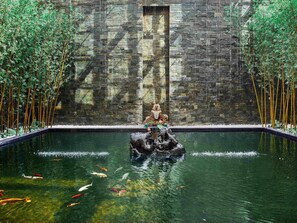A koi pond with a statue in the center, surrounded by bamboo plants.