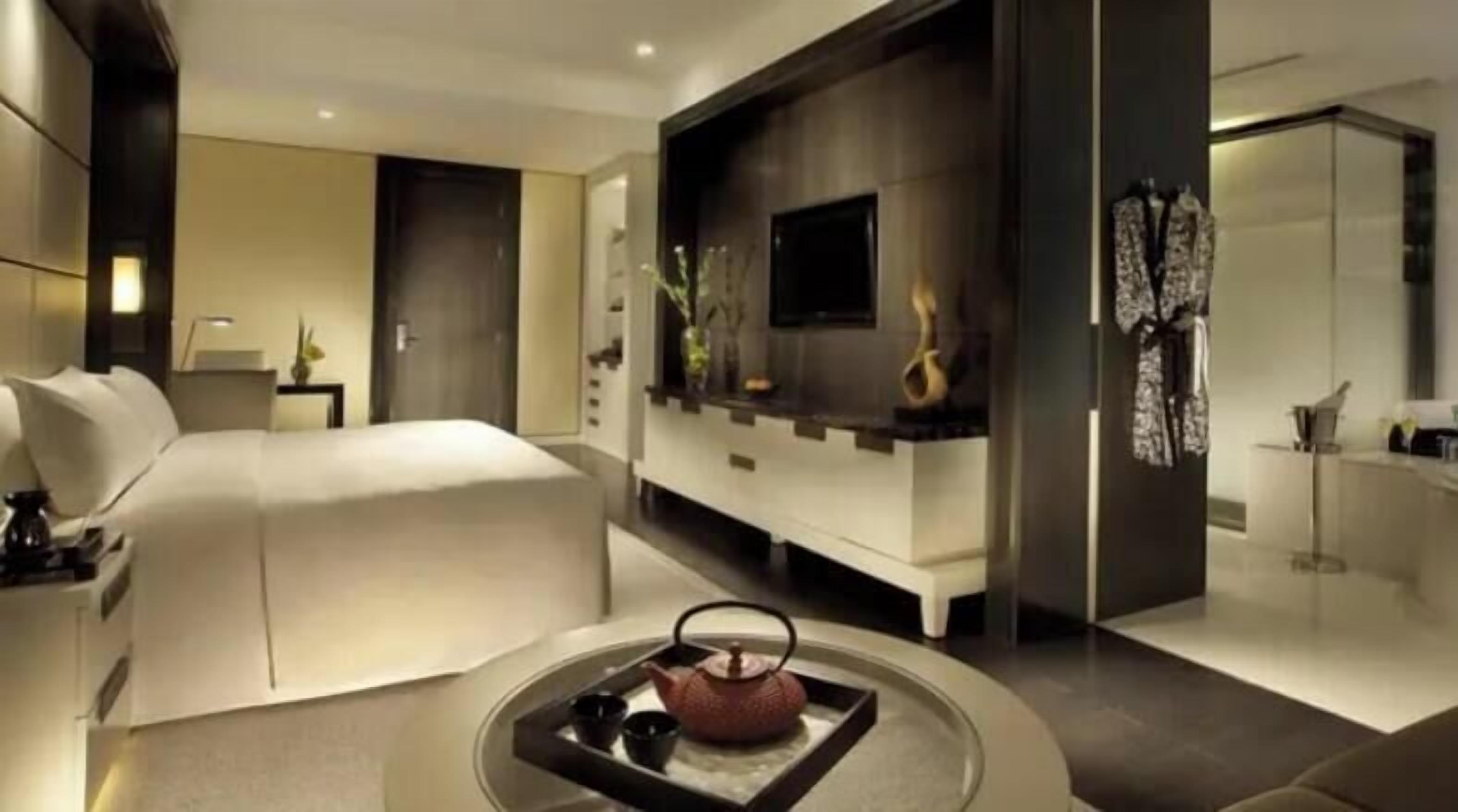 A modern hotel room with a large bed, a seating area with a table, a flat-screen TV, and a decorative wall.