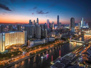 A cityscape at dusk with high-rise buildings, a river, and a bridge.