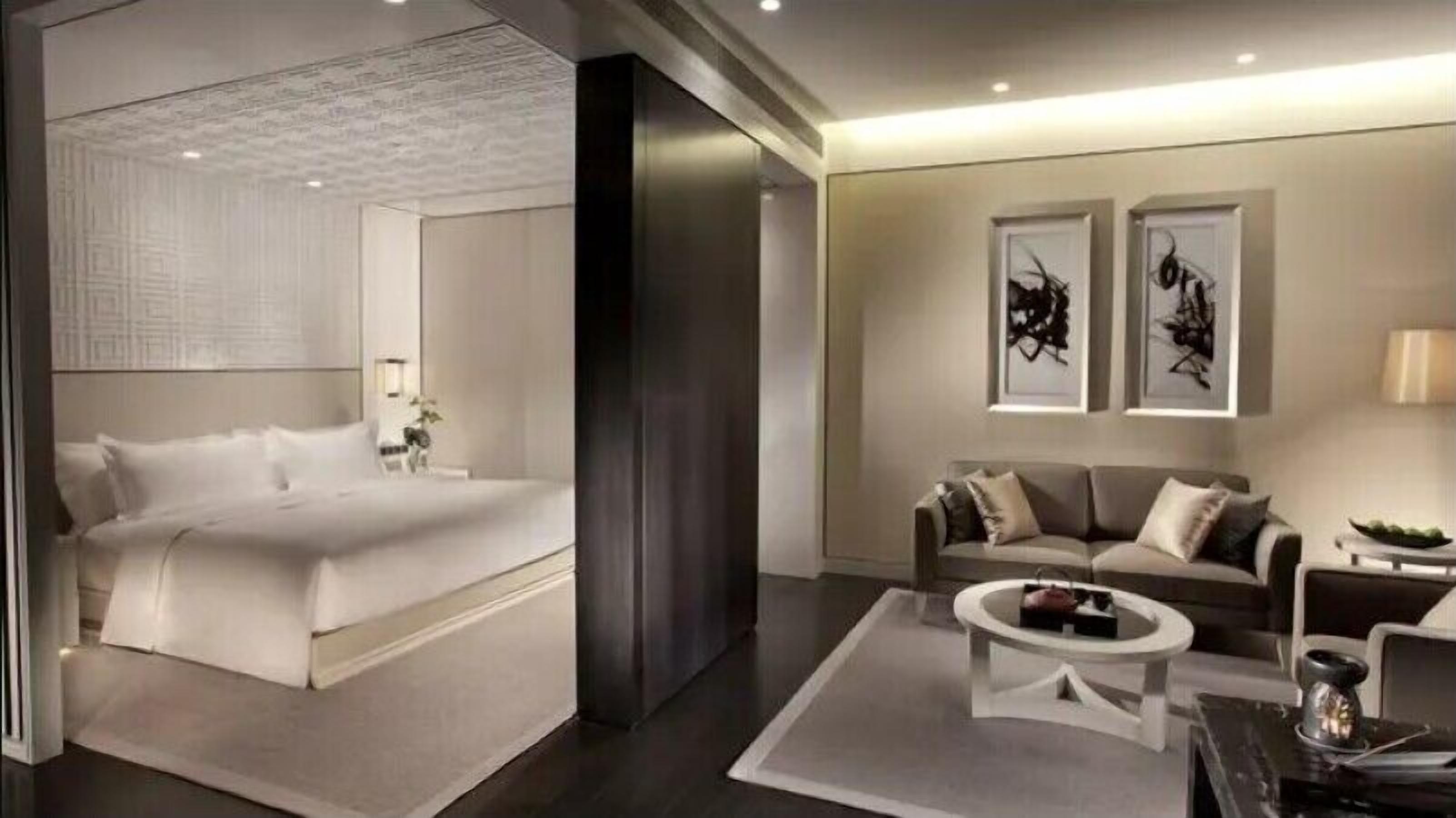 A modern hotel room with a large bed, a sofa, a coffee table, and artwork on the walls.