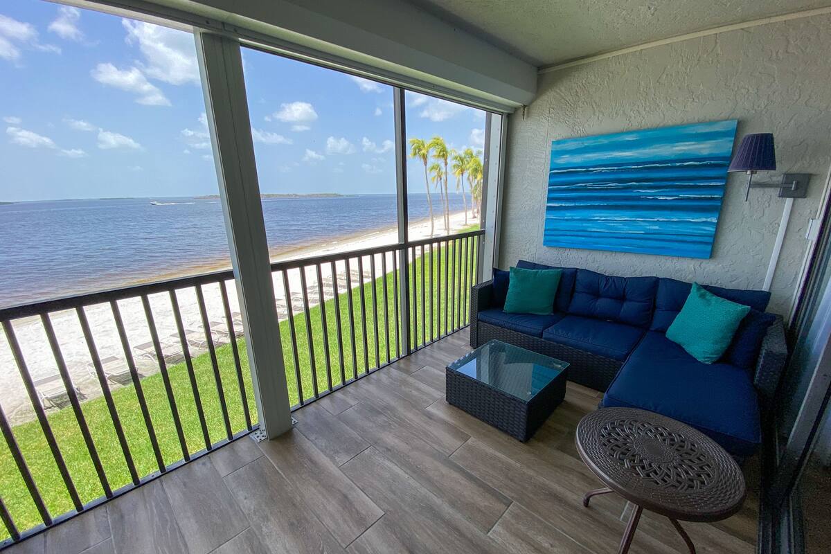 A balcony with a view of the beach, a sofa, a coffee table, and a lamp.