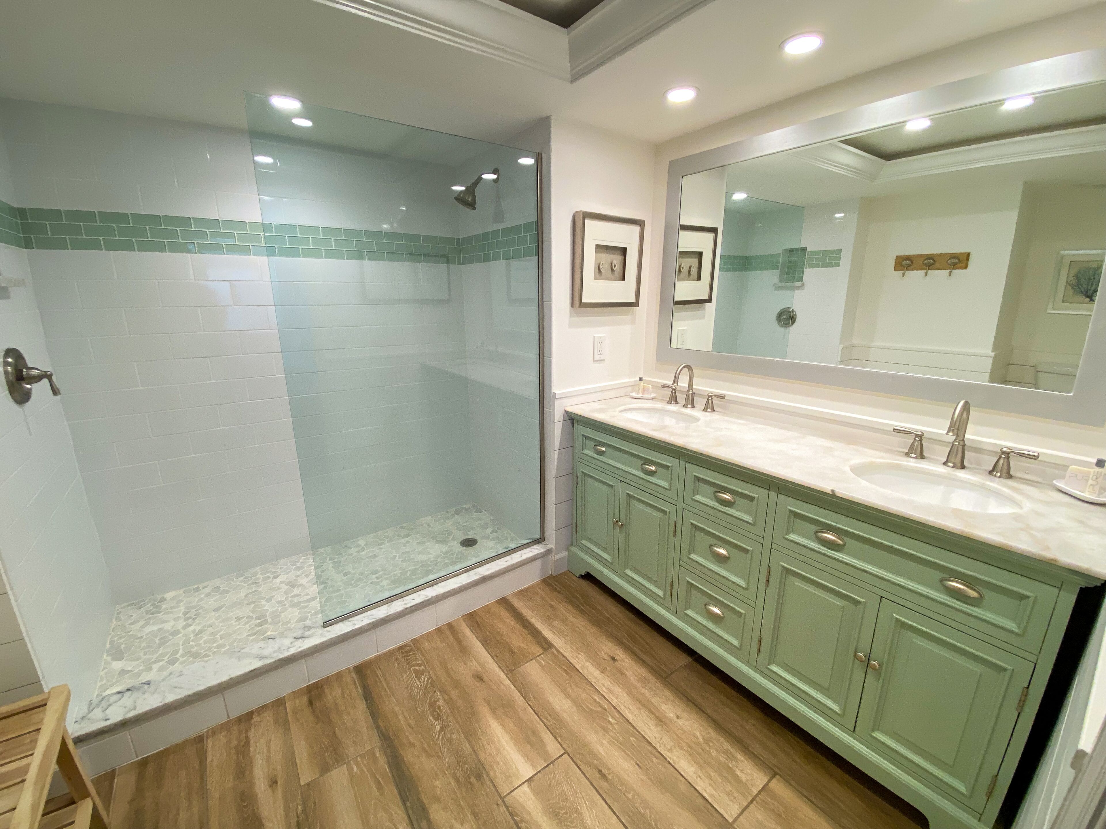 A modern bathroom with a glass-enclosed shower, a large vanity with a mirror, and wooden flooring.
