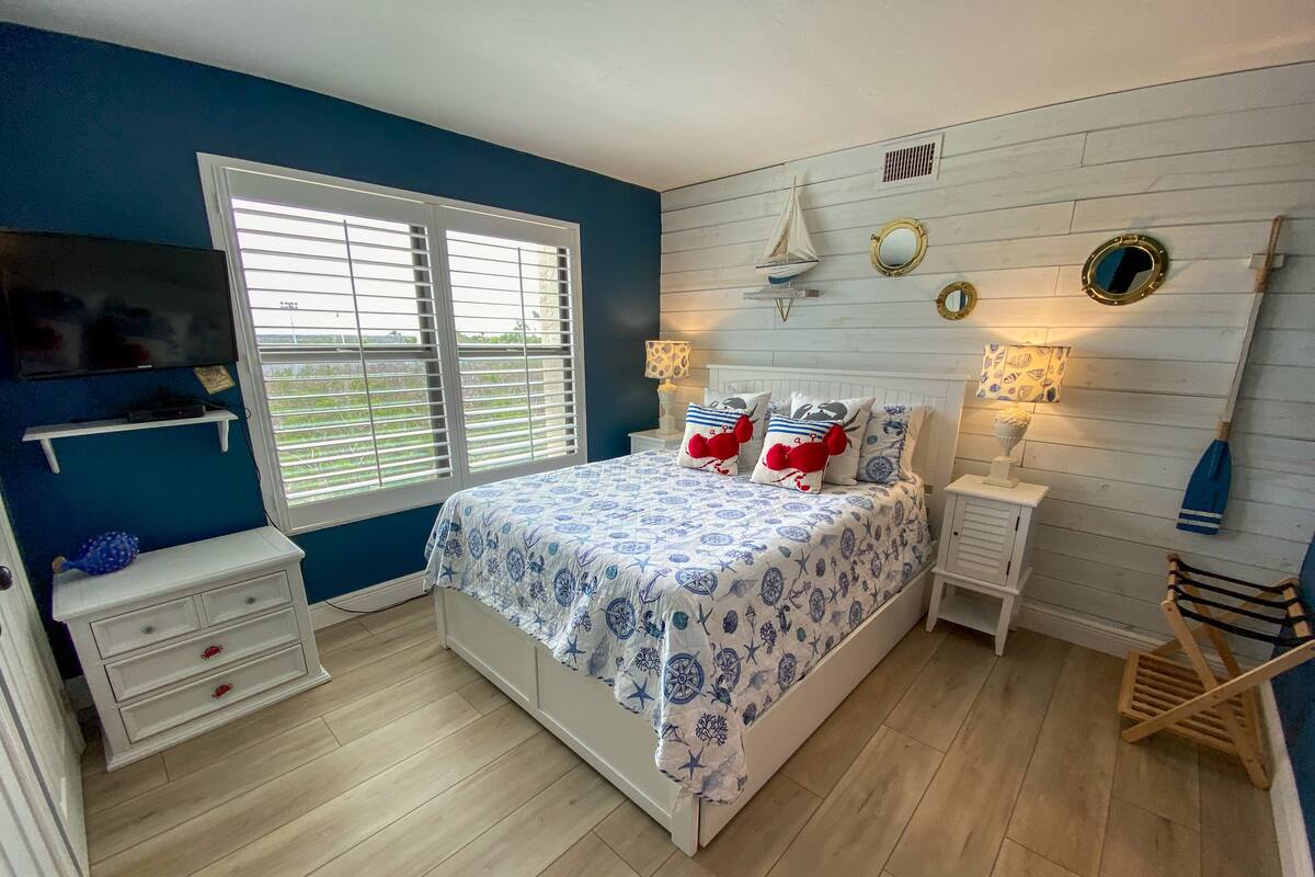 A bedroom with a bed, a TV, a window, and a wooden floor.