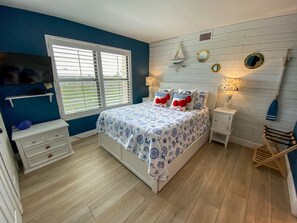 A bedroom with a bed, a TV, a window, and a wooden floor. - Resort Harbour Properties (Fort Myers)