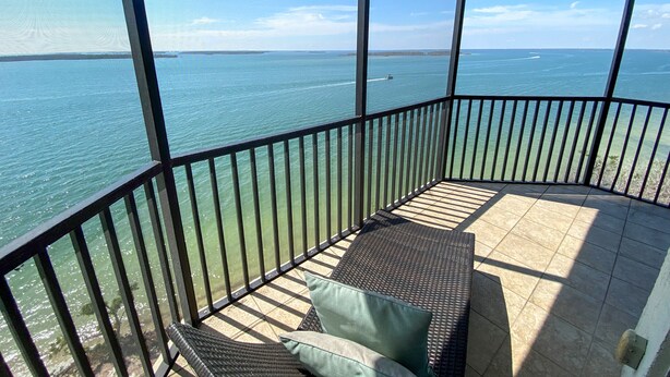A balcony with a view of the sea, a wicker sofa with cushions, and a tiled floor. - Resort Harbour Properties (Fort Myers)
