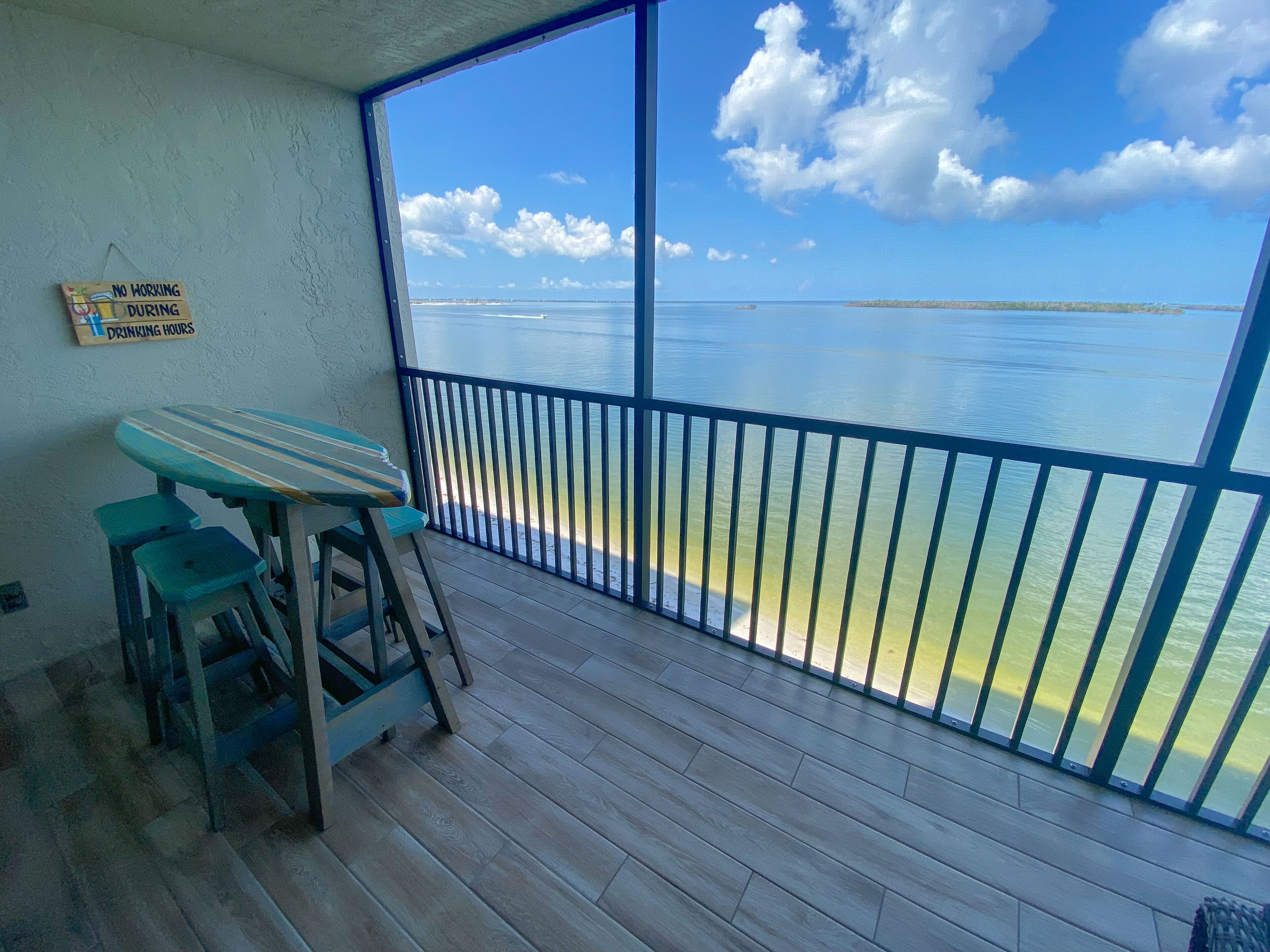 A balcony with a view of the sea, a wooden table, and two stools.