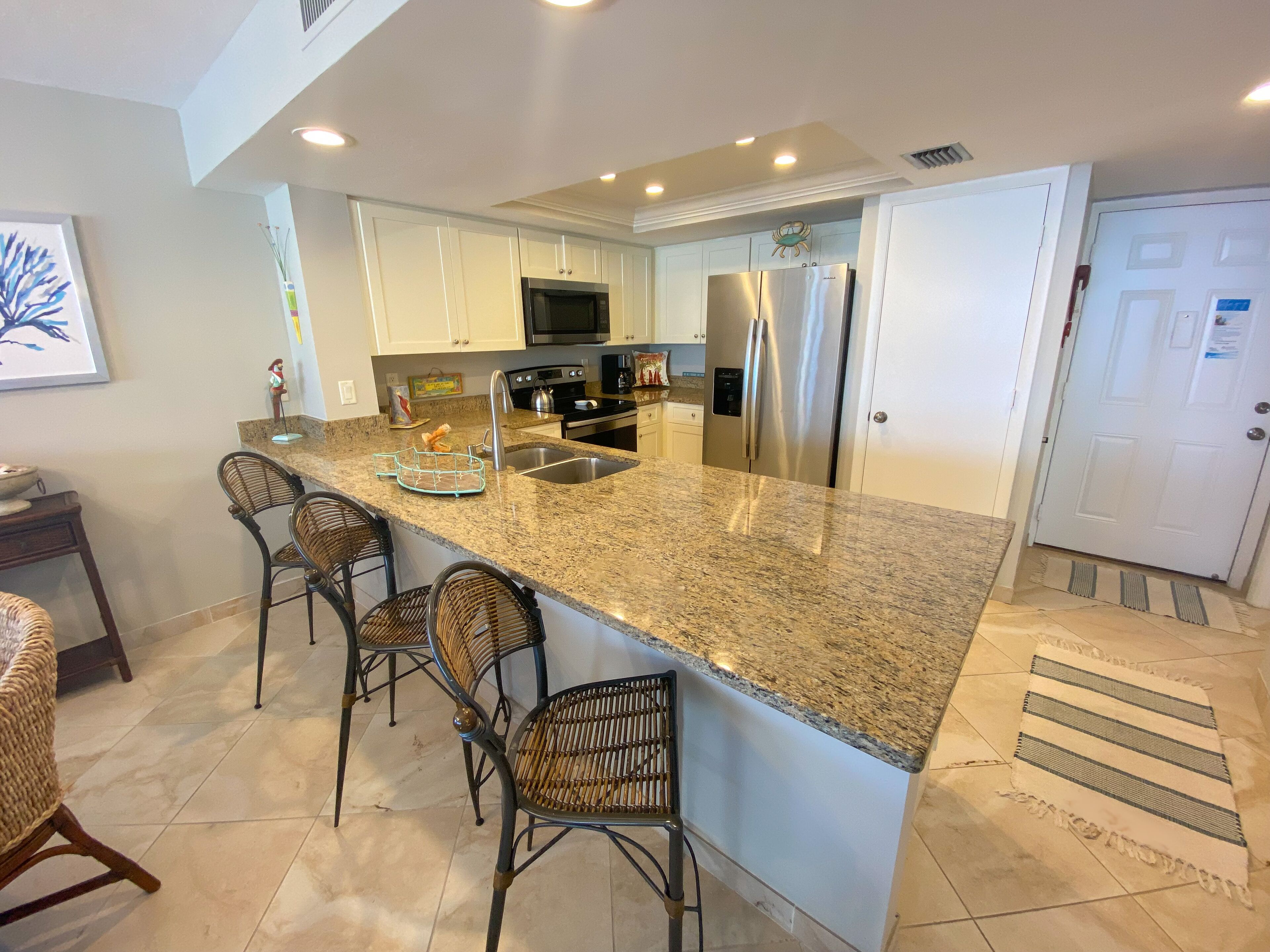 A modern kitchen with granite countertops, stainless steel appliances, and a breakfast bar with wicker chairs.