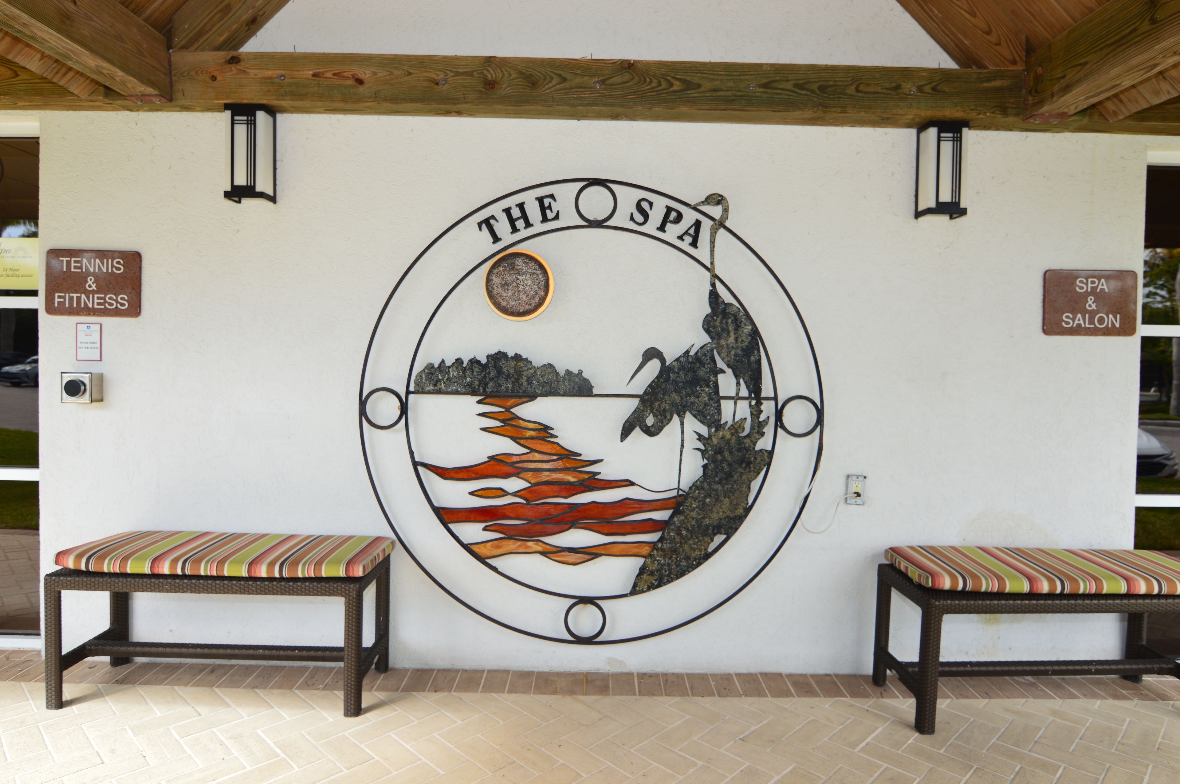 Un mur orné d’un logo circulaire représentant « The Spa », et deux bancs avec des coussins à rayures.