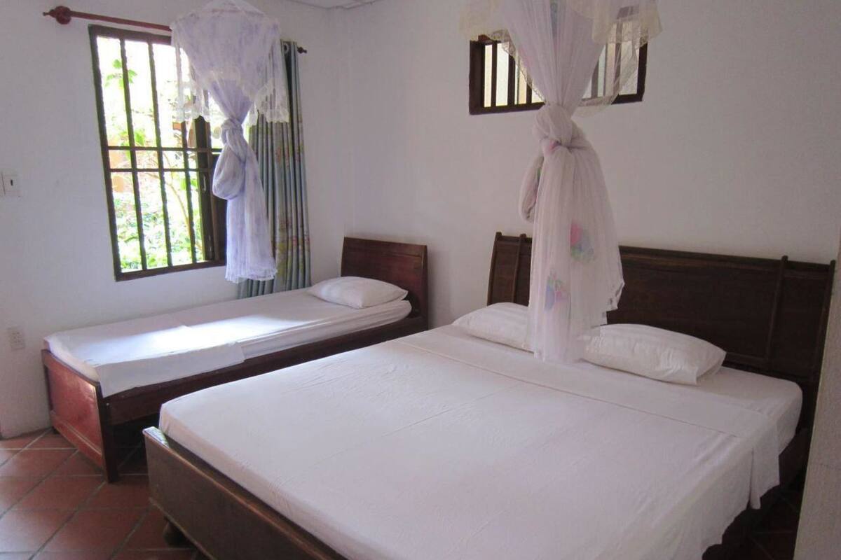 A room with two single beds, a window with curtains, and a mosquito net over one bed.