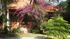 Ett traditionellt hus med ett halmtak, omgivet av frodig grönska och blommande växter.