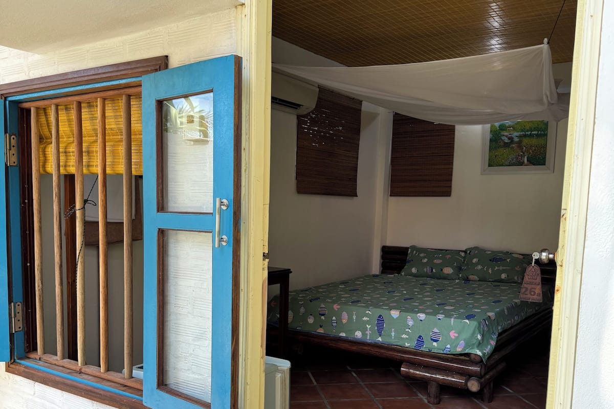 A room with a bed, a window with wooden bars, a white canopy, and a tiled floor.