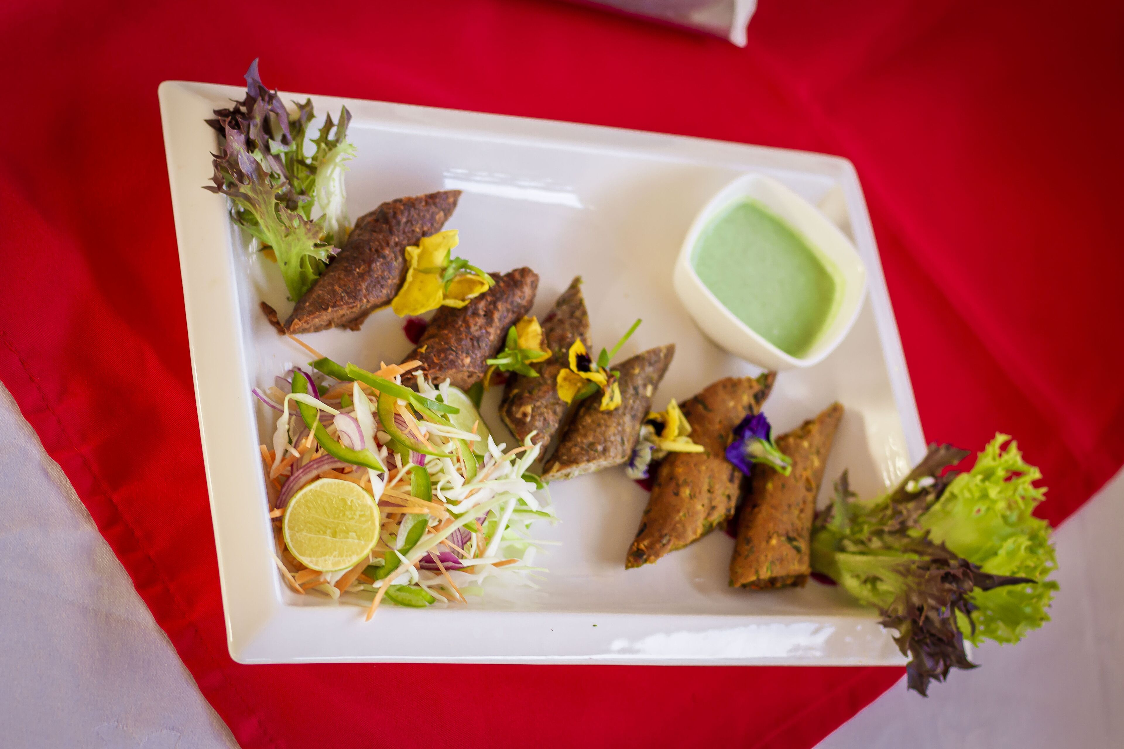 A rectangular white plate with food items including grilled meat, salad, and a green sauce.