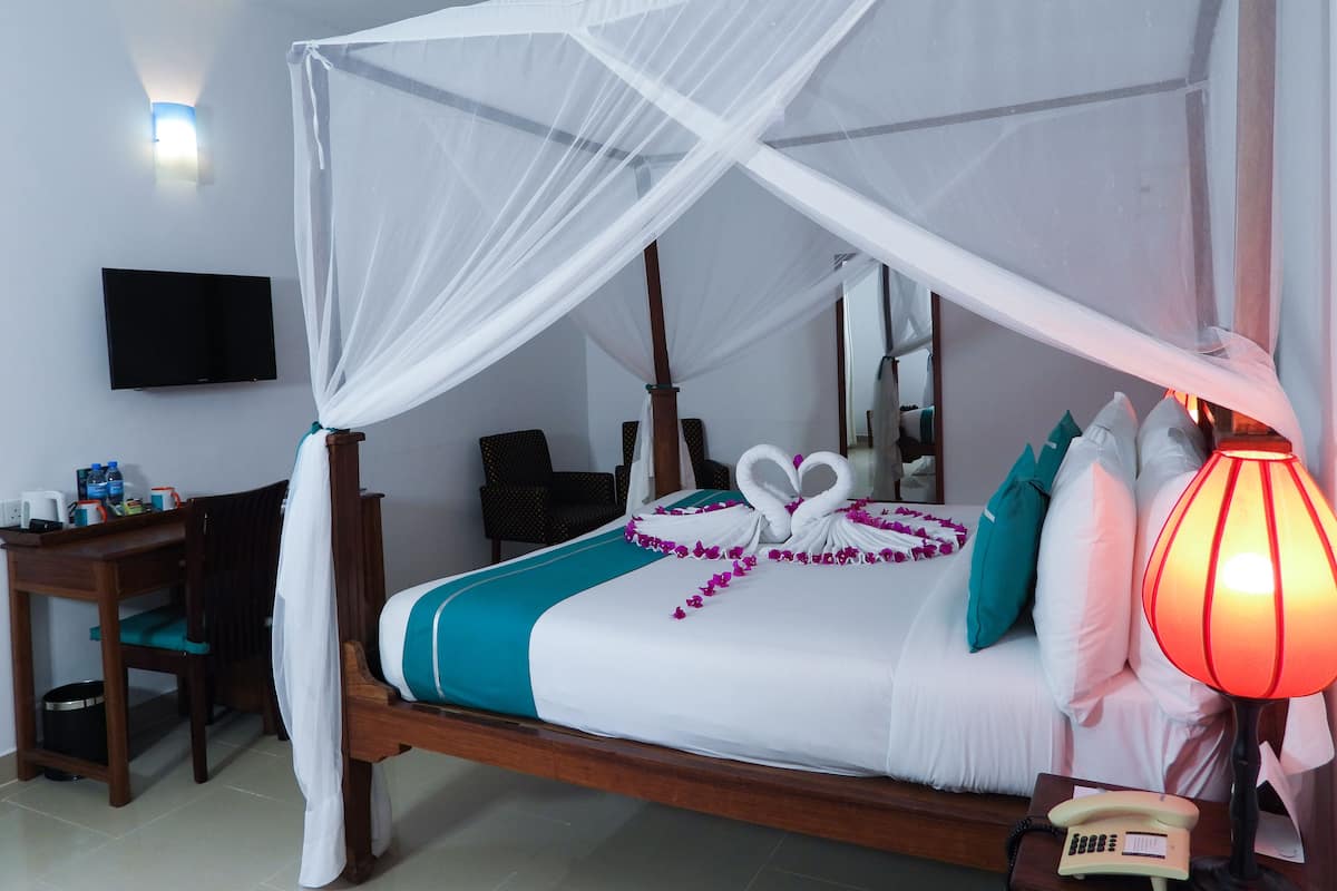 Une chambre d’hôtel équipée d’un lit, d’un bureau, d’une chaise, d’un téléphone, d’une télévision et d’une lampe de chevet.