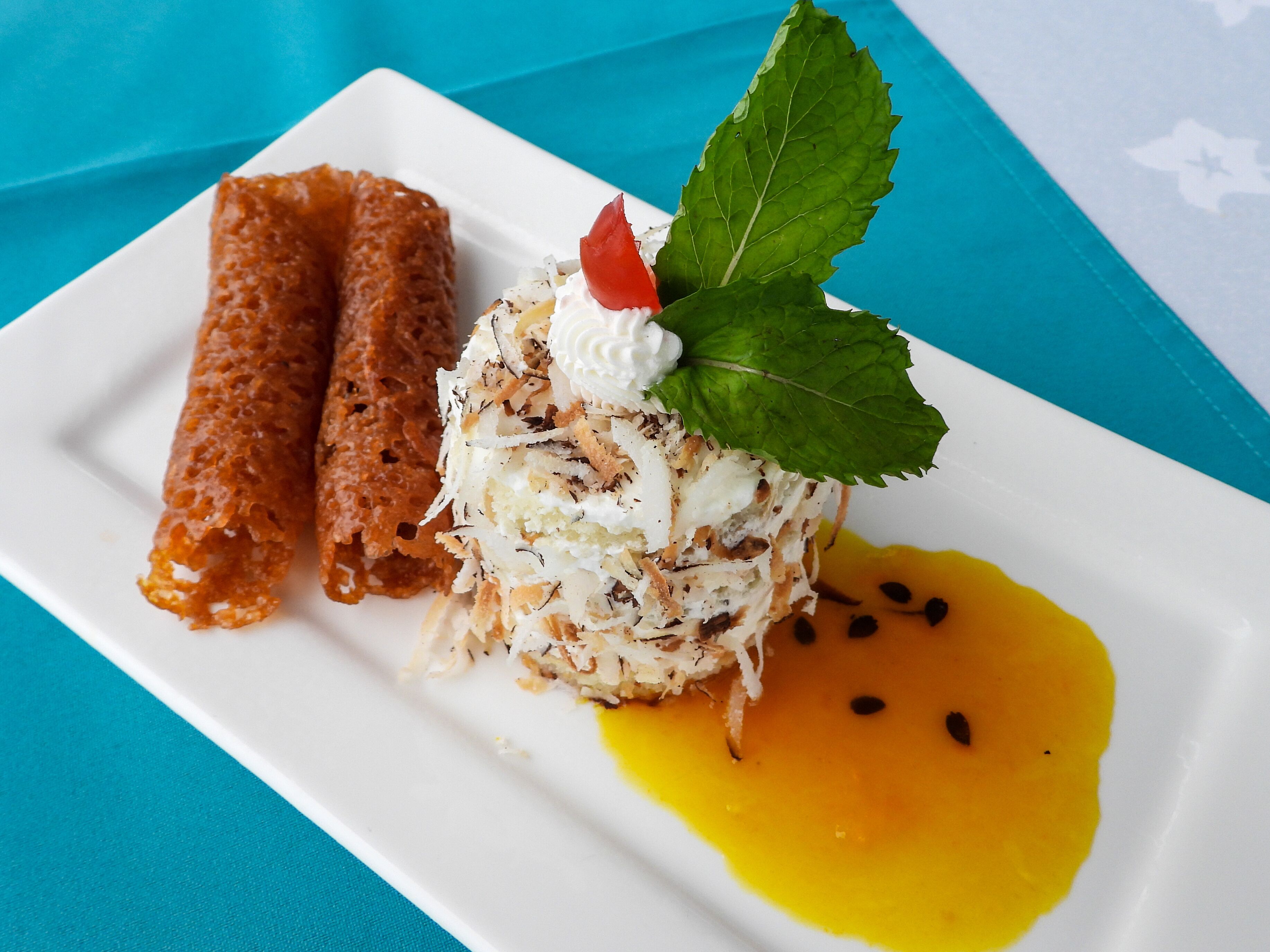 A plate with a dessert consisting of a rolled pastry, a layered dessert with whipped cream and a mint leaf, and a yellow sauce.