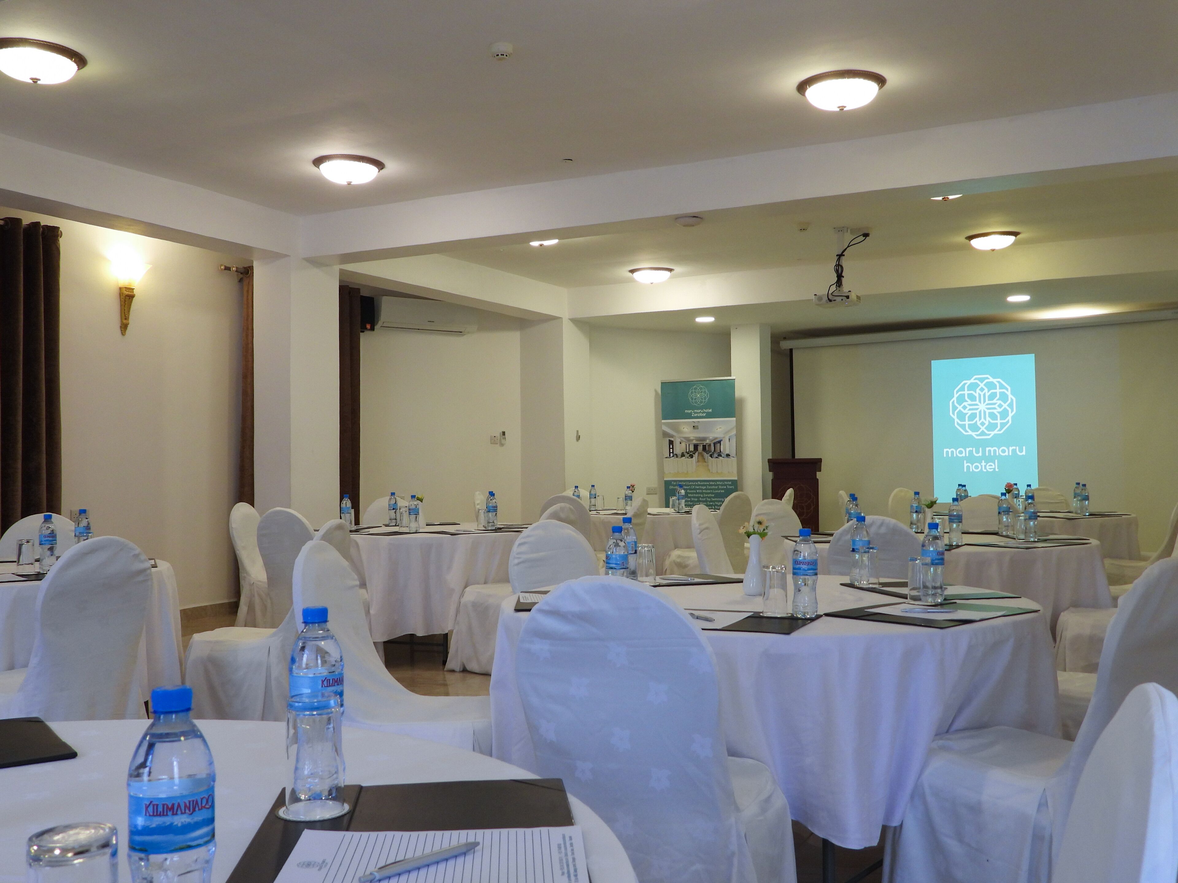 A conference room with round tables, white chairs, and water bottles.