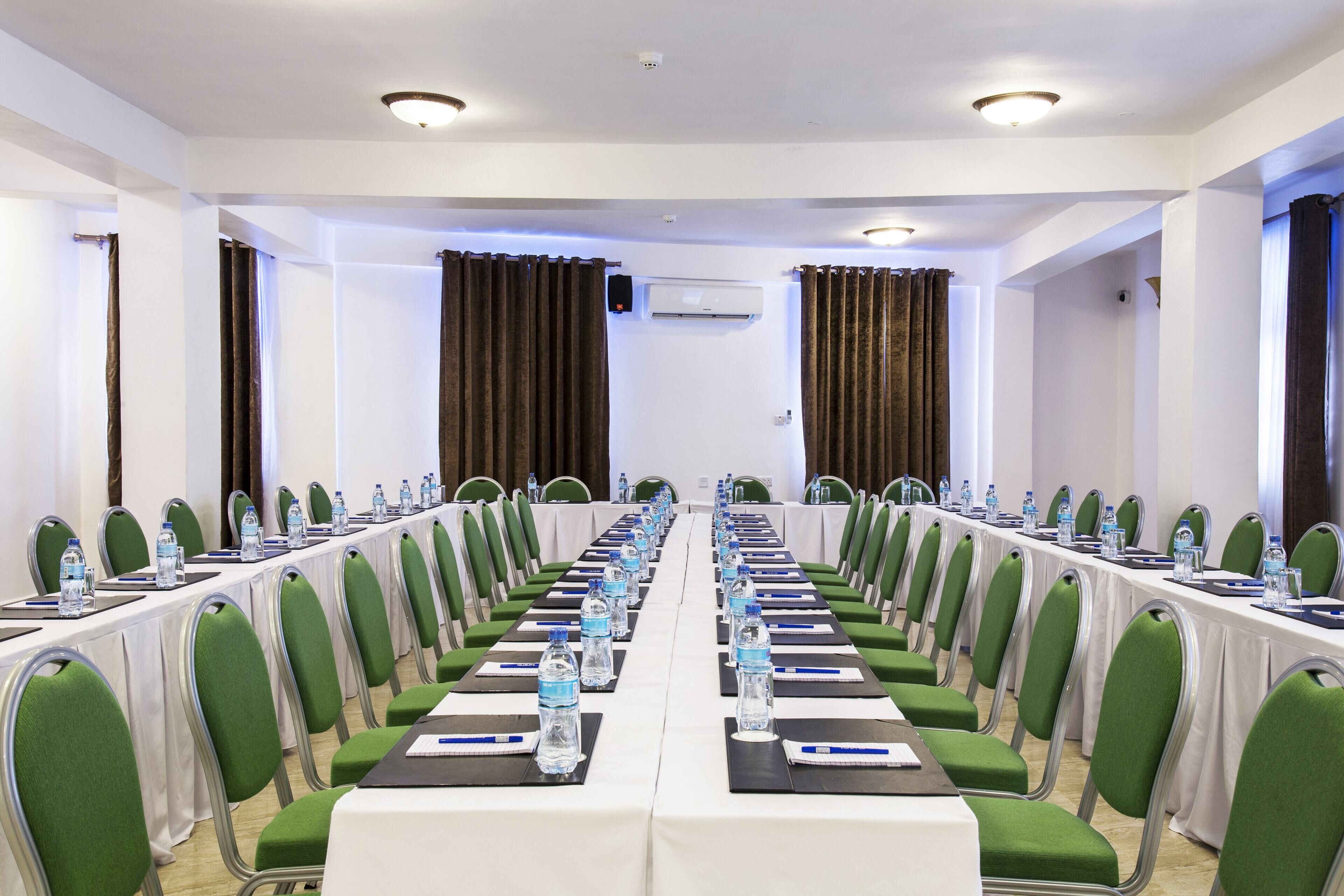 Ein Konferenzraum mit langem Tisch, grünen Stühlen, Wasserflaschen und einer weißen Tischdecke.