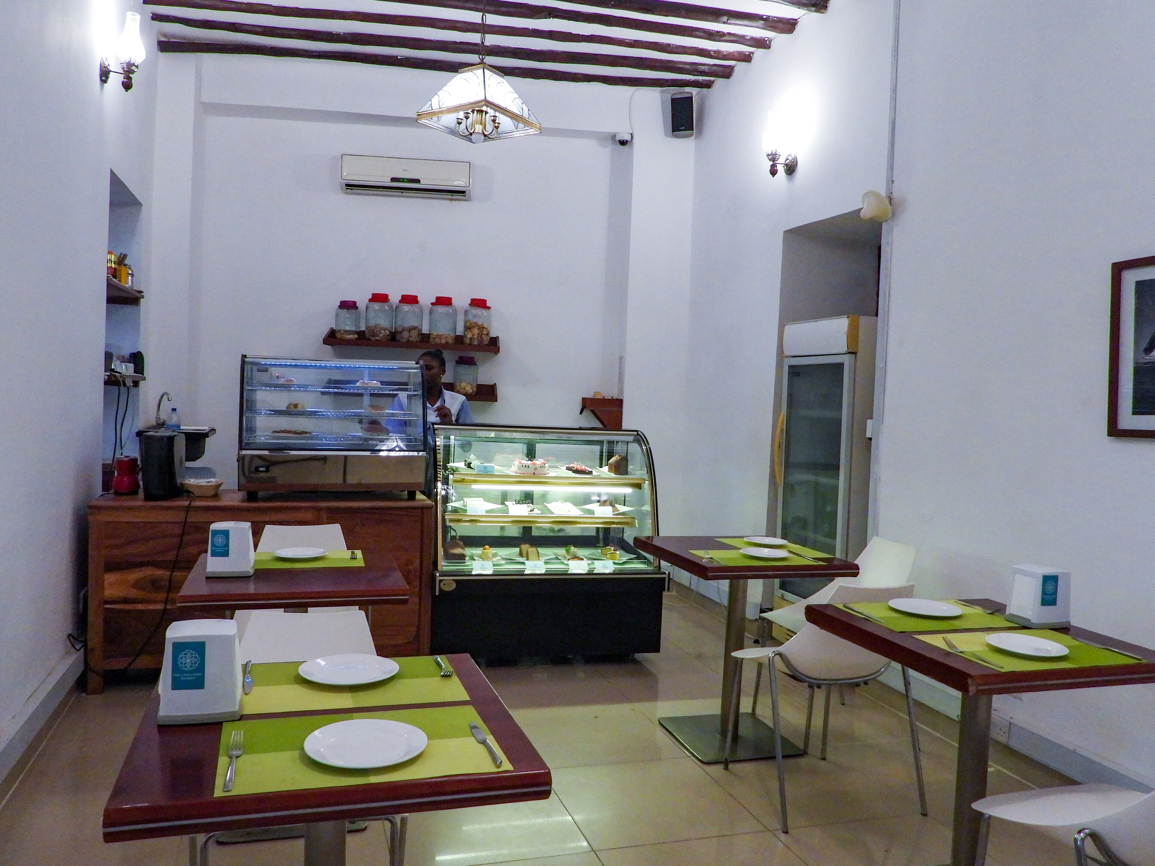 A restaurant with tables set for dining, a display case with desserts, and a ceiling fan.