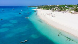 A beach with clear turquoise waters, boats, and a white sandy shore. - Maru Maru Hotel (Zanzibar Town)