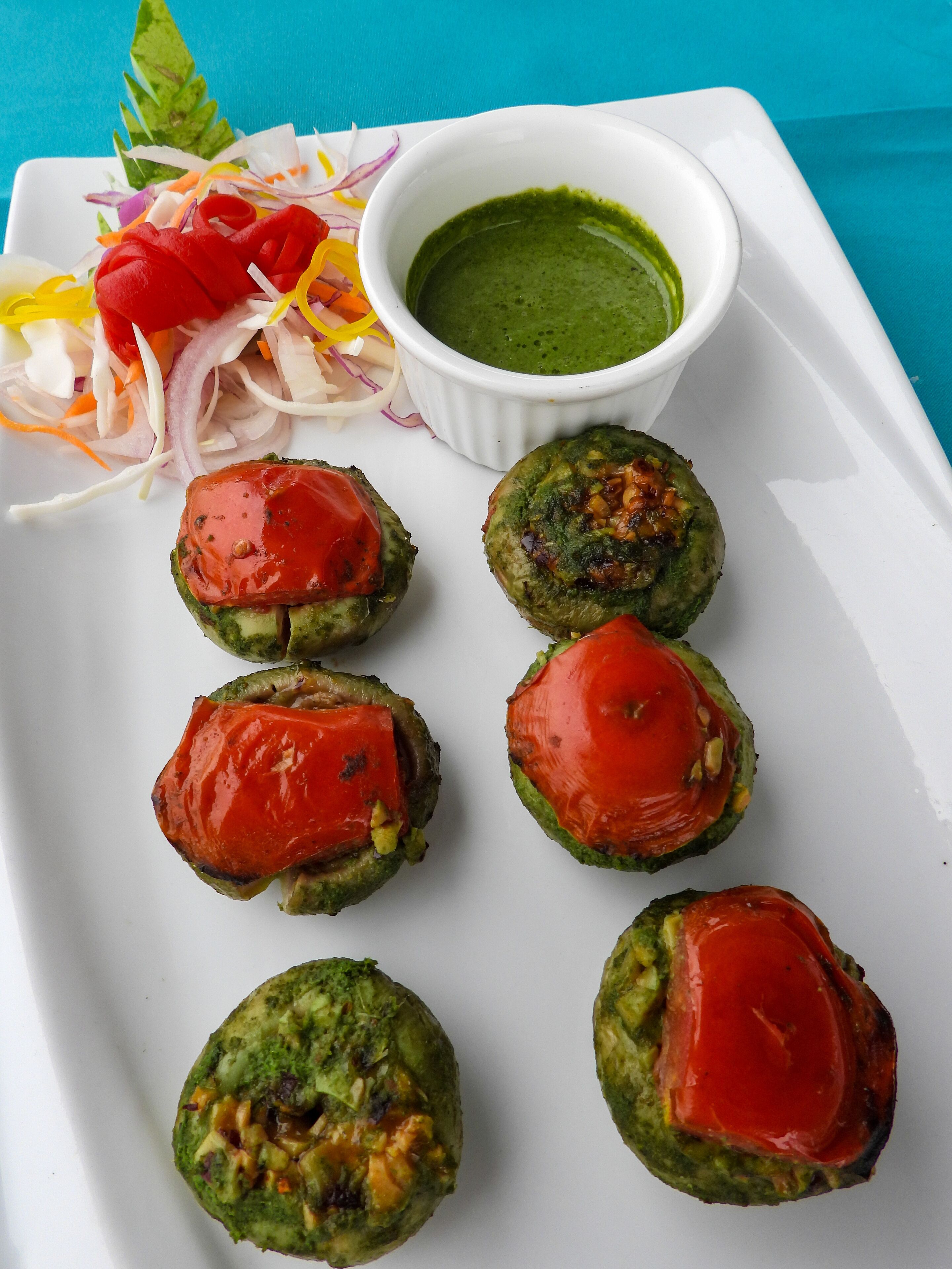 A plate with six vegetable patties topped with tomato slices, a side salad, and a bowl of green sauce.