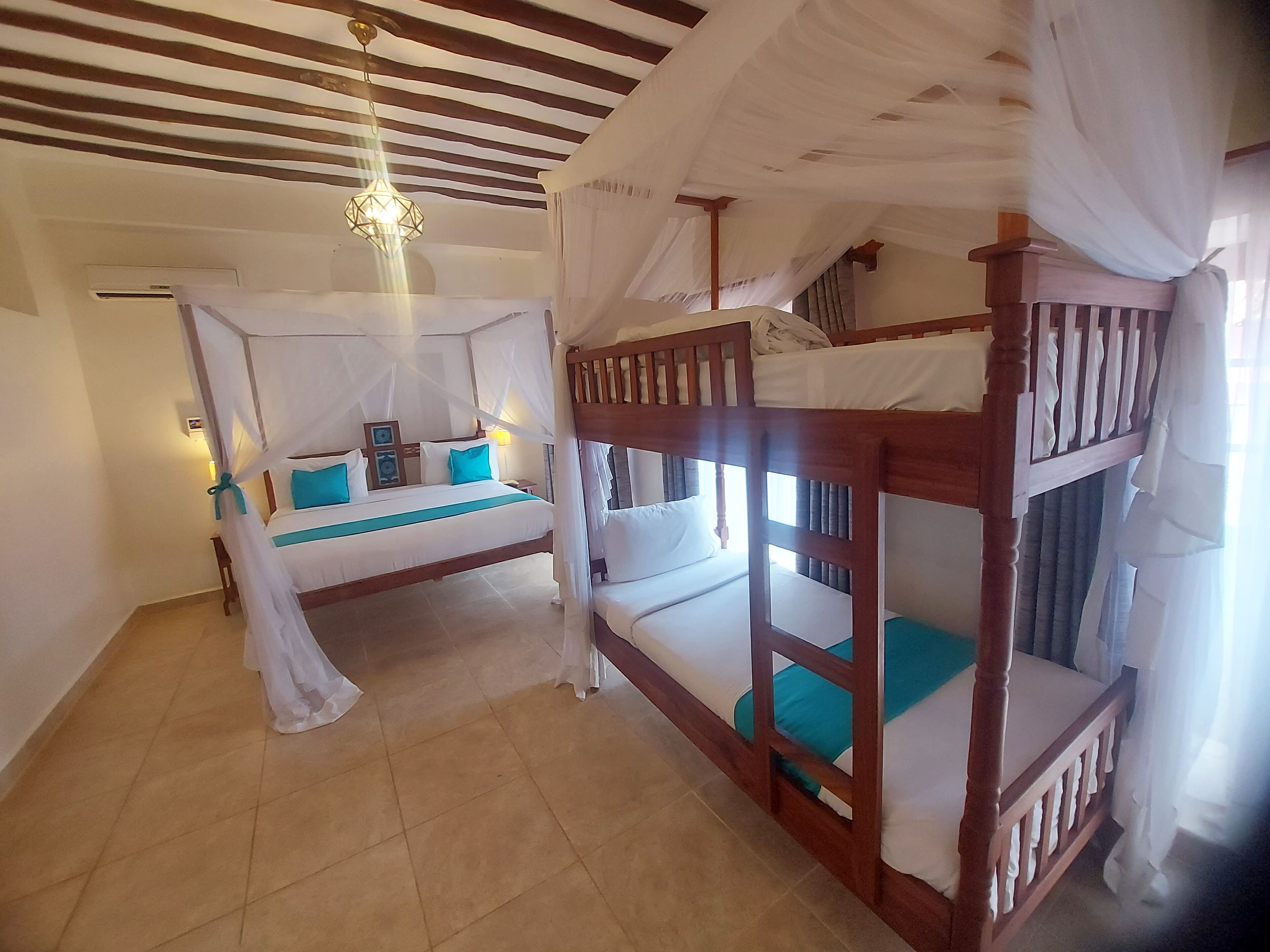 A room with a bed under a canopy, a wooden bunk bed, and a chandelier.