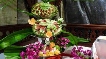 A table with a fruit arrangement, including a watermelon centerpiece, surrounded by plates of food and utensils.