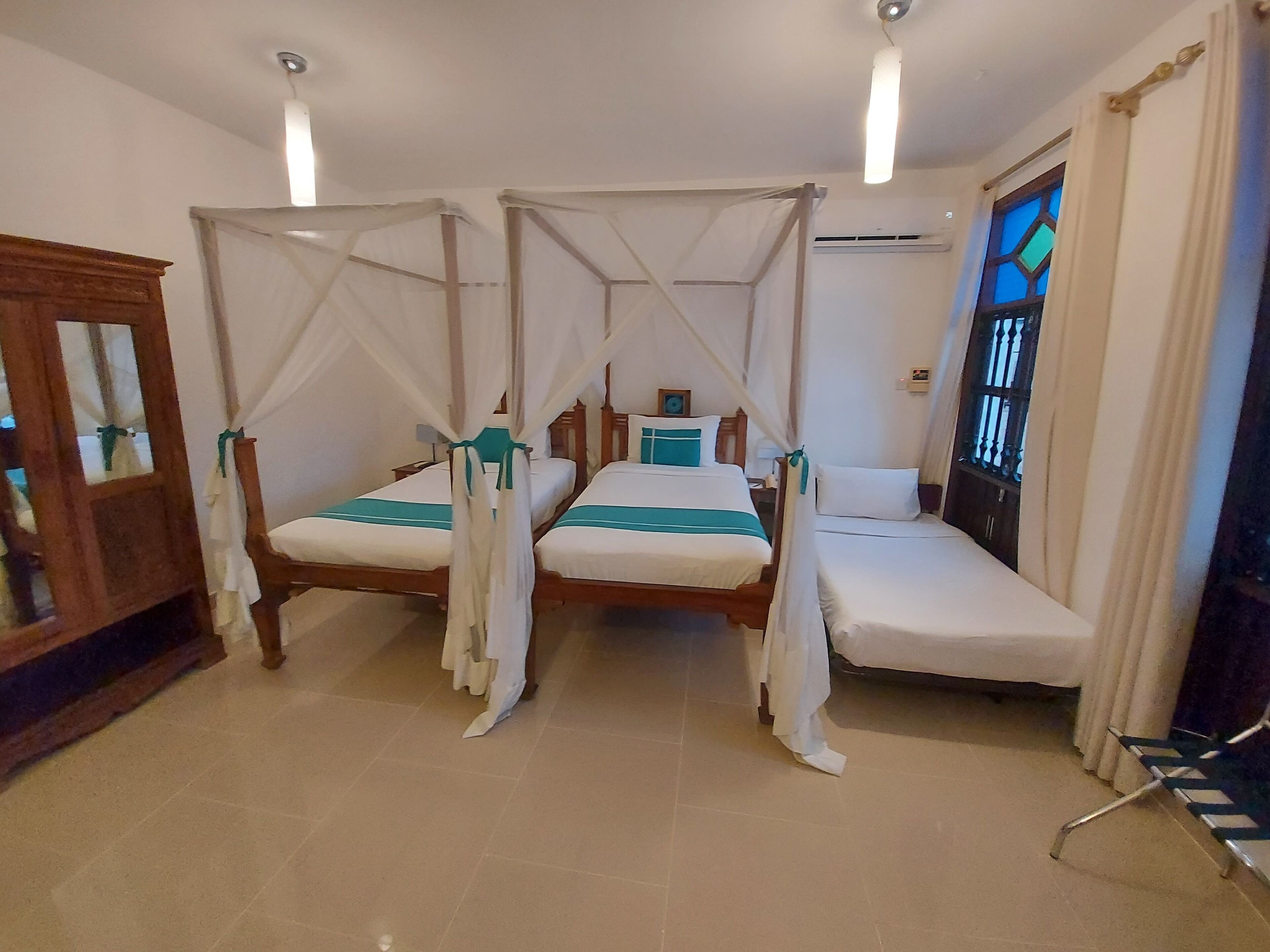 A room with two beds, each with a canopy, a wooden cabinet, and a window with bars.