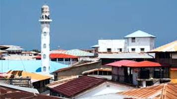 Uma área costeira com um farol branco imponente, vários edifícios com telhados coloridos e um céu azul límpido.