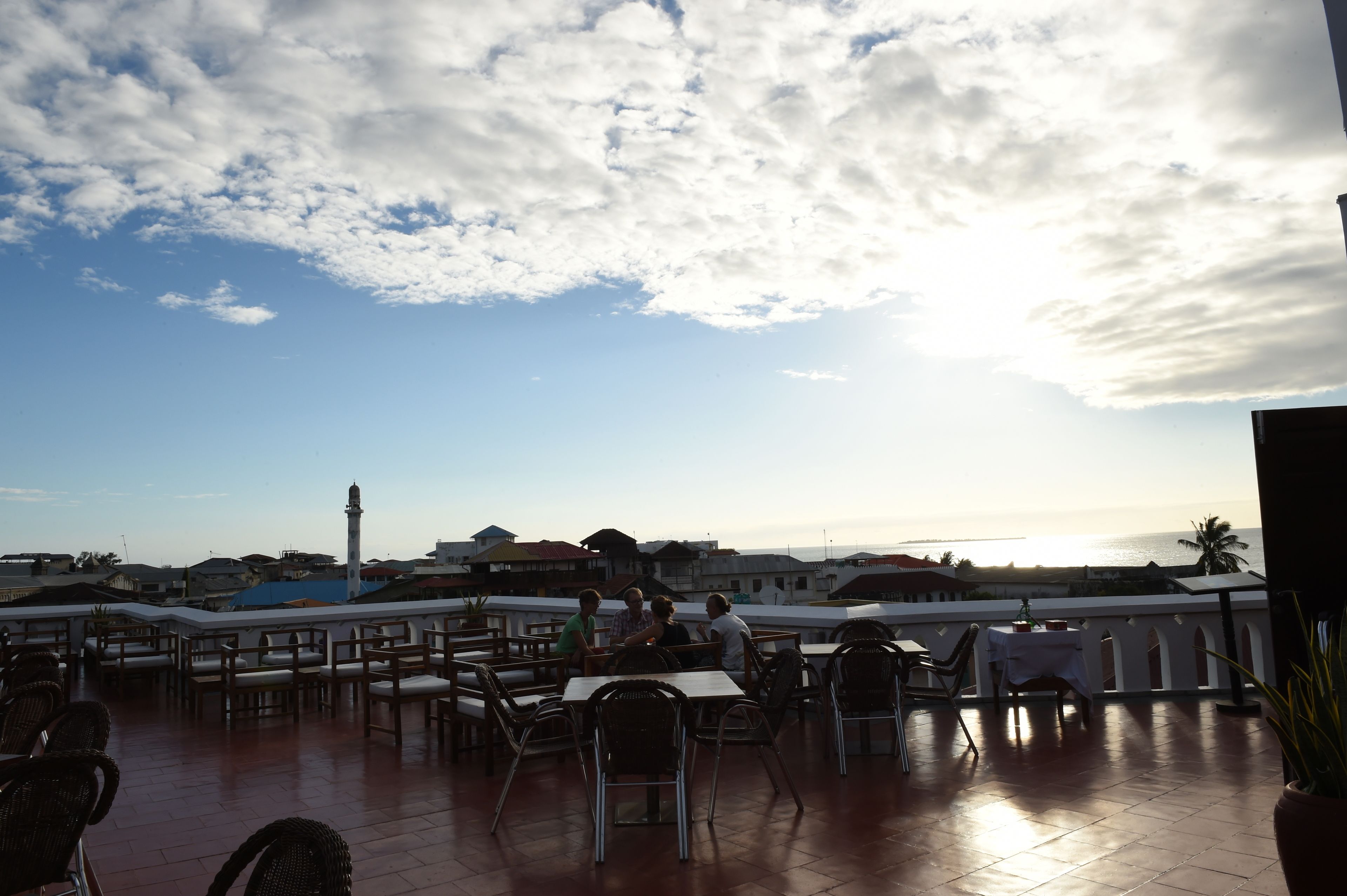An outdoor dining area with tables and chairs, overlooking a coastal view with buildings and a lighthouse in the distance.
