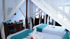 A room with two beds, each with a canopy and a flower arrangement. There is a desk and a chair in the corner. - Maru Maru Hotel (Zanzibar Town)