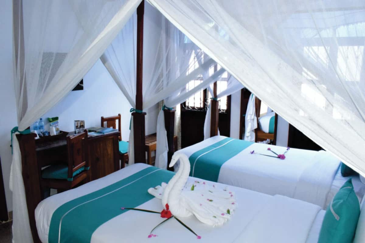 Une chambre avec deux lits, chacun doté d’un baldaquin et agrémenté d’un arrangement floral. Un bureau et une chaise se trouvent dans un coin de la pièce.