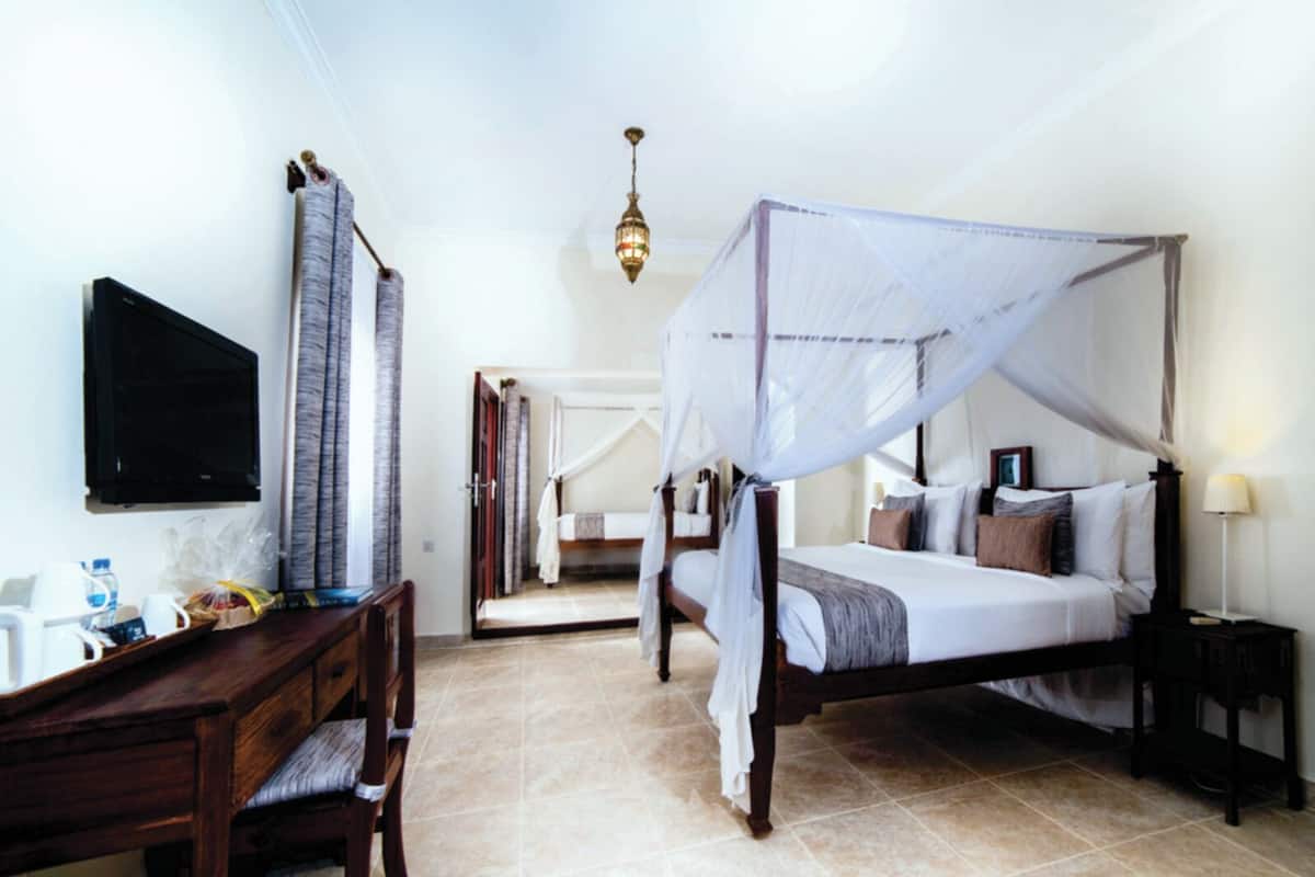Une chambre à coucher avec un lit à baldaquin, un bureau avec une chaise, une télévision et une table de chevet avec une lampe.
