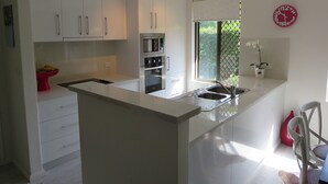Una cocina moderna con armarios blancos, electrodomésticos de acero inoxidable, una isla grande con pileta y una ventana con vista a follaje.
