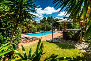 Una piscina con sillas de descanso, rodeada de abundante follaje y un jacuzzi.