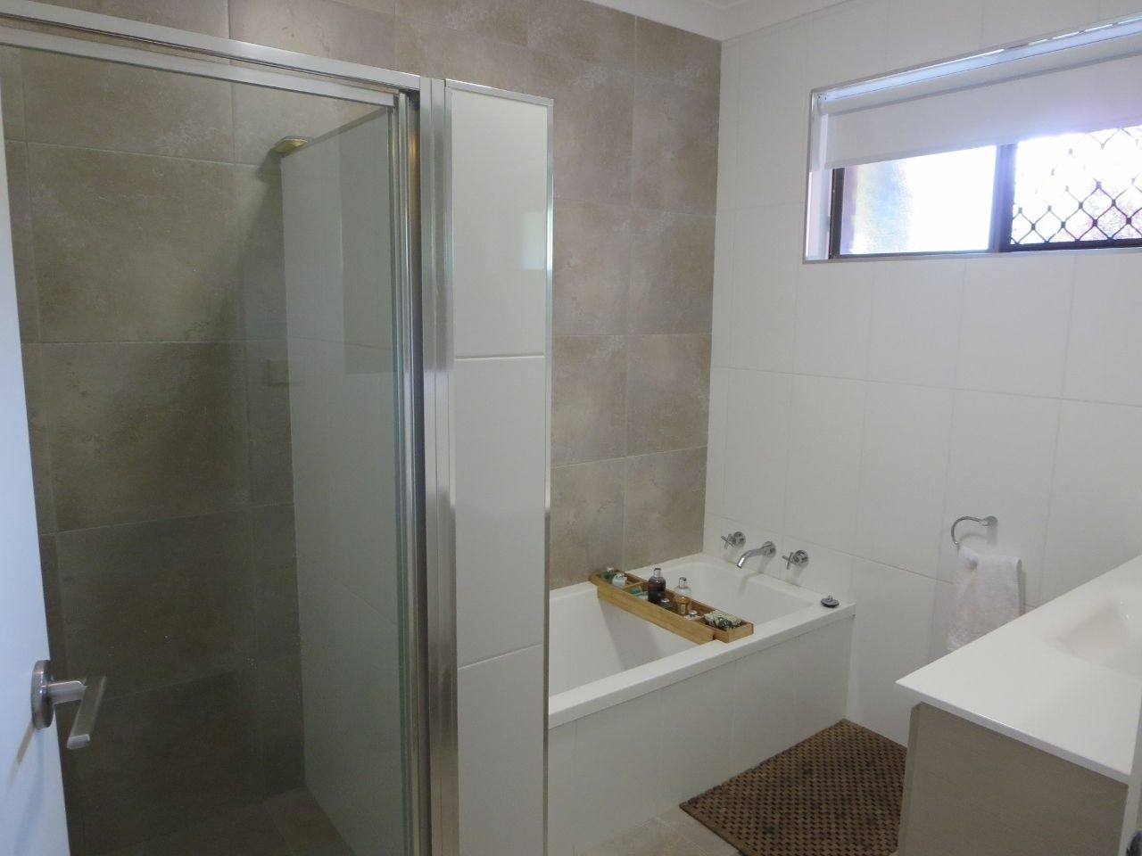 A bathroom with a glass shower enclosure, a bathtub with a wooden tray, and a white sink.