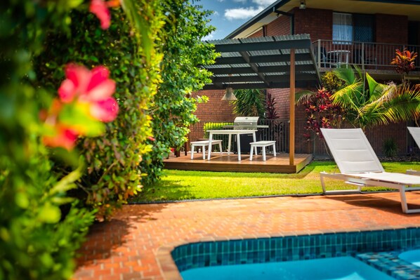 Un patio trasero con una barbacoa, piscina y un porche cubierto.