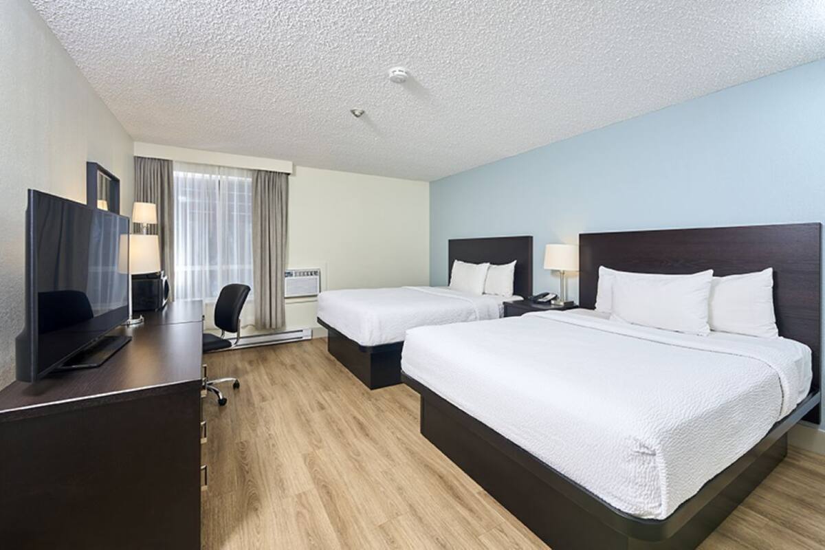 A hotel room with two beds, a desk with a computer, a TV, and a window with curtains.