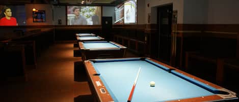 A pool table area with multiple tables, a projector screen, and a pool cue.