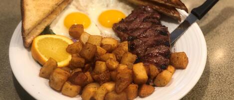 Un plato de comida para el desayuno con tostadas, huevos, filete y papas.
